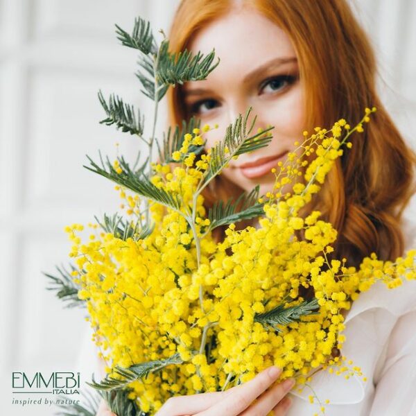 Γυναίκα κρατάει κίτρινα λουλούδια στα χέρια της και χαμογελάει